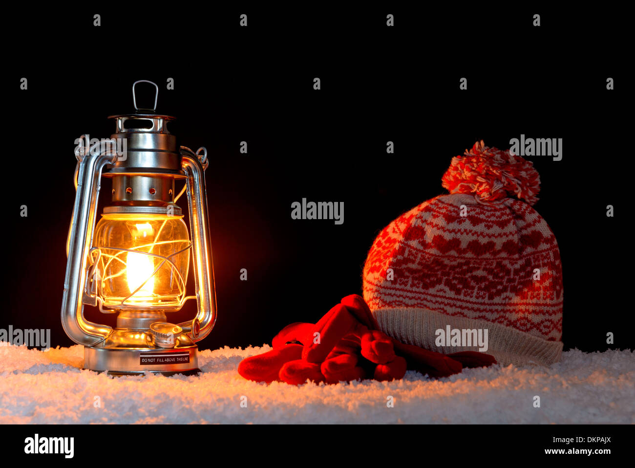 Une lanterne à huile sur la neige avec un bobble hat et gants, fond noir. Banque D'Images