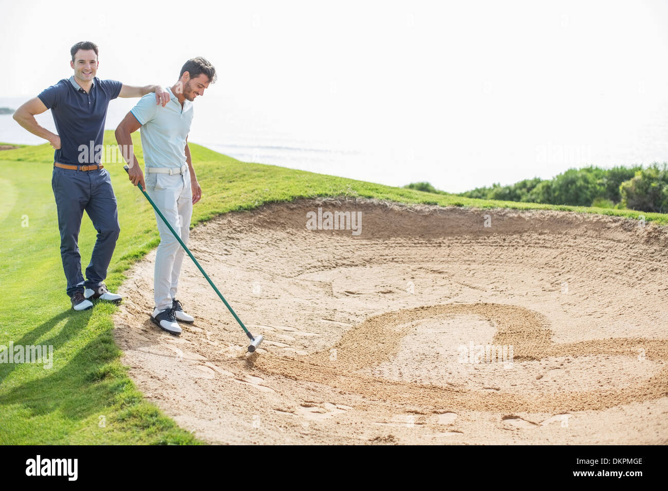 Men raking heart-shape en fosse de sable on golf course Banque D'Images