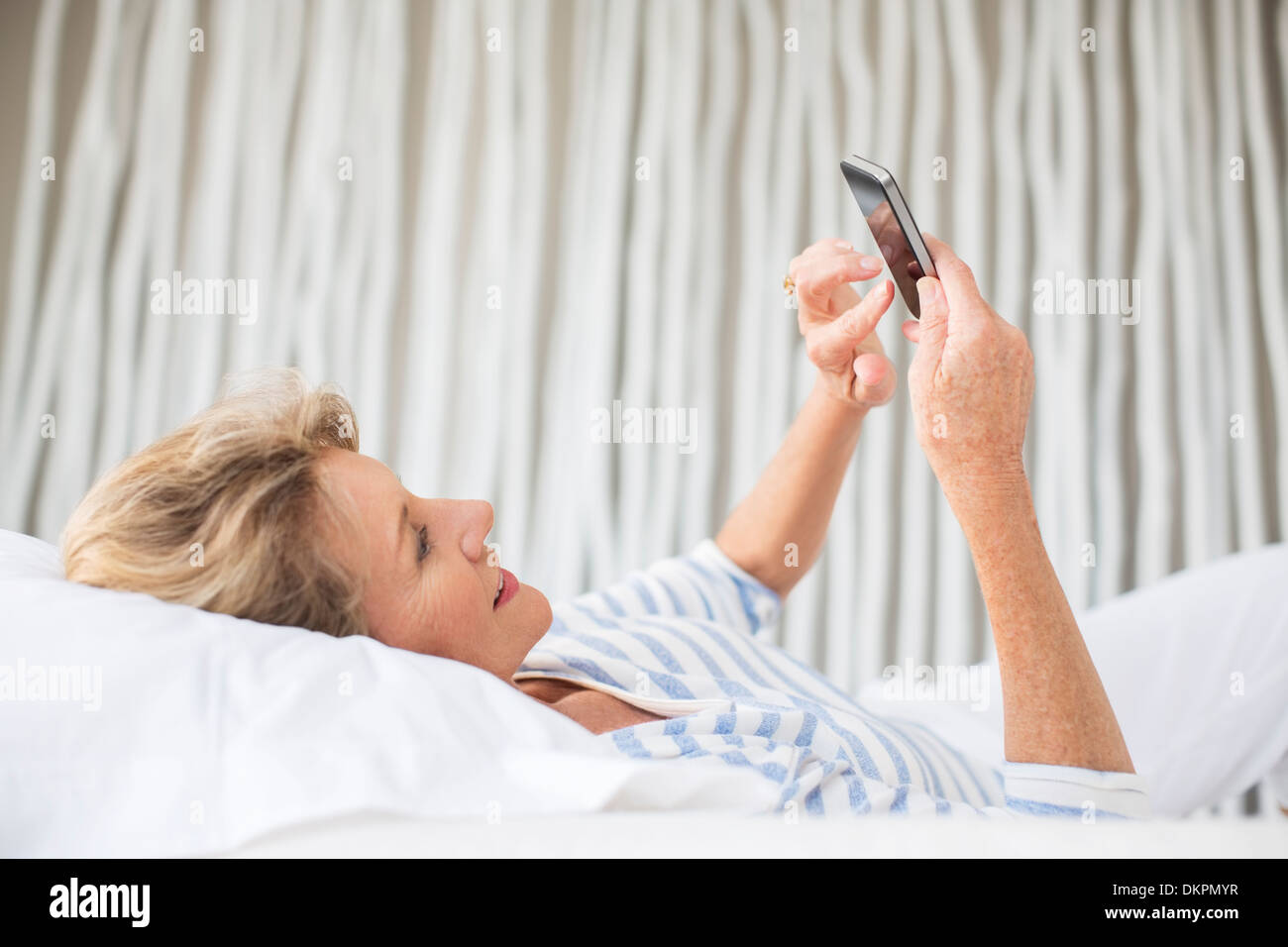Femme plus âgée using cell phone on bed Banque D'Images