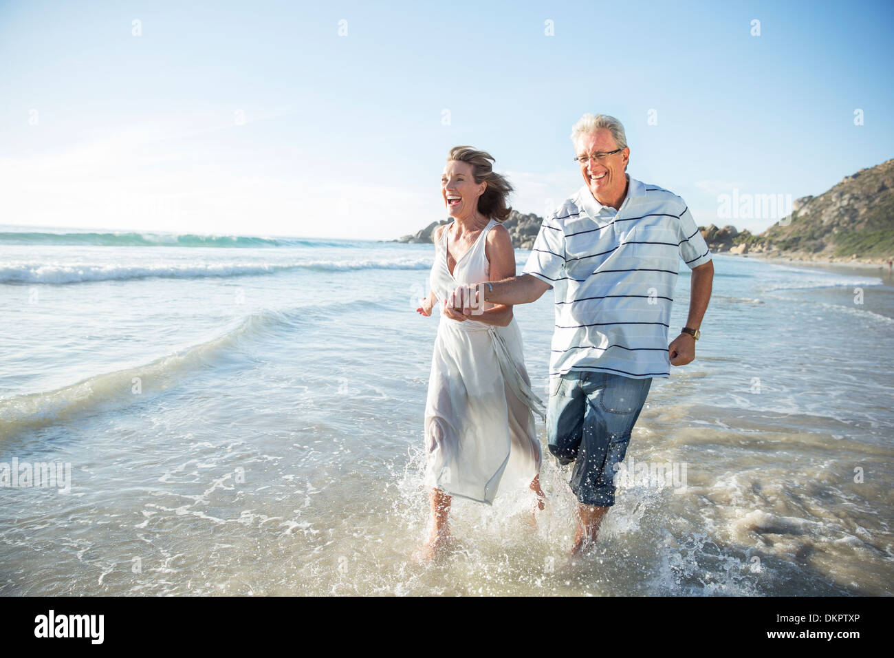 Vieux couple jouant dans les vagues sur la plage Banque D'Images