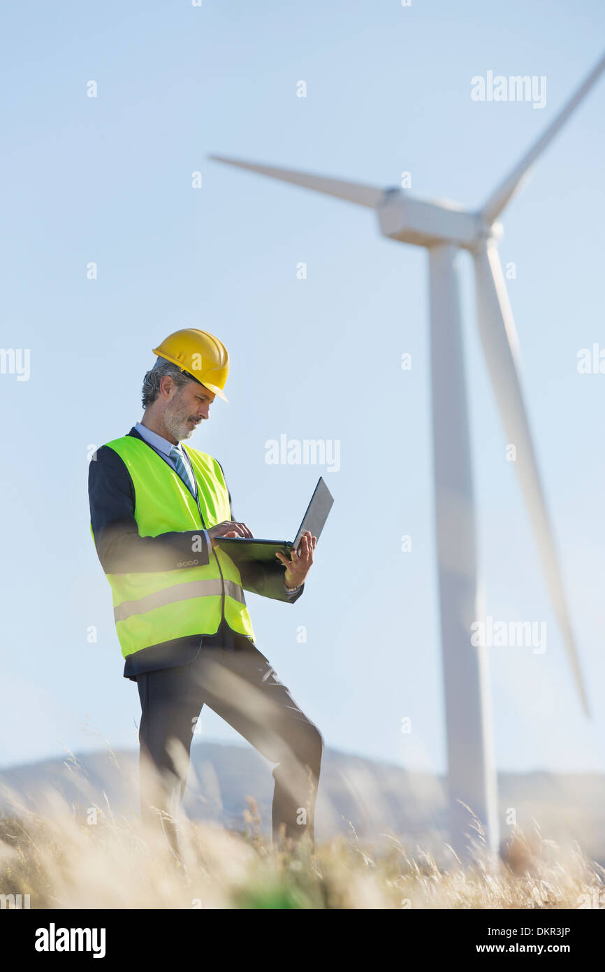 Worker using laptop by wind turbine in rural landscape Banque D'Images