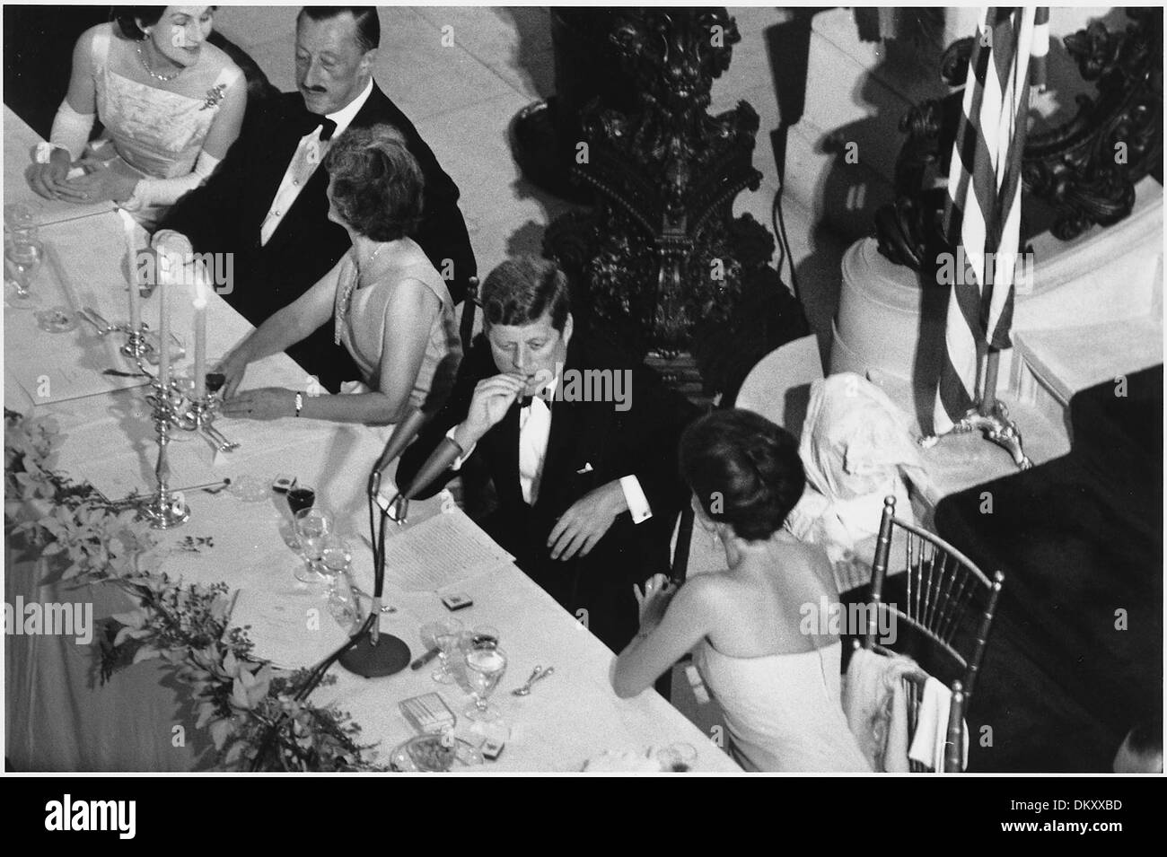 Cette photographie capture le président John F. Kennedy et la première dame Jacqueline Kennedy lors d'un dîner de la Coupe de l'America à Newport, Rhode Island, qui s'est tenu au « The Breakers ». Divers dignitaires et personnalités ont assisté à l'événement, célébrant la prestigieuse course de yachts. Banque D'Images