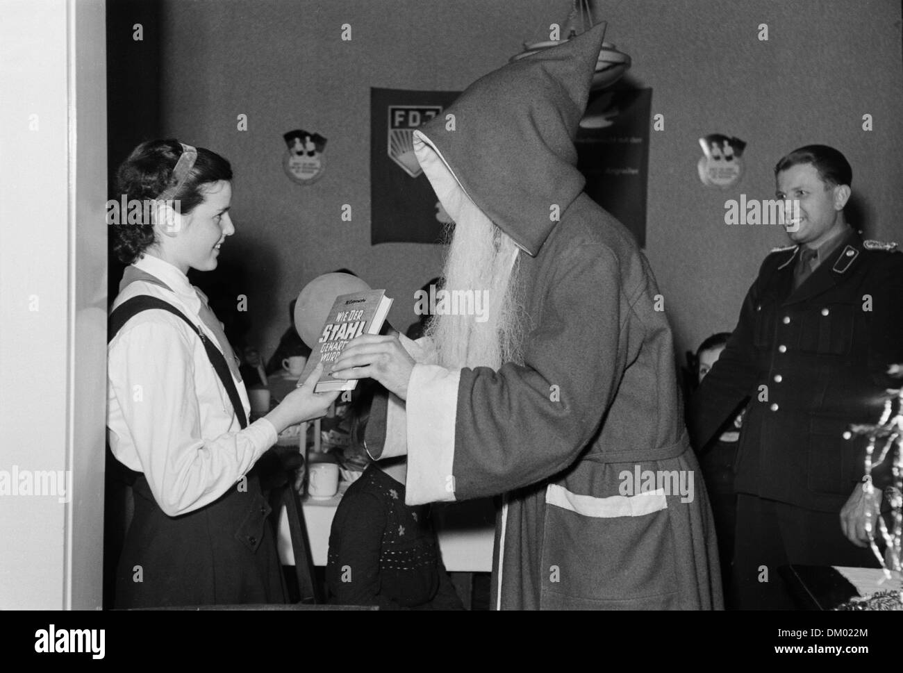 Une fille dans un uniforme pionniers Jeunes reçoit le livre 'Wie der Stahl gehärtet wurde" (Comment l'acier était hardenend) comme cadeau de Noël du Père Noël au cours de la célébration de Noël de la Volkspolizei à Leipzig, Allemagne, sans date (4091, 1952). Photo. Deutsche Fotothek Banque D'Images