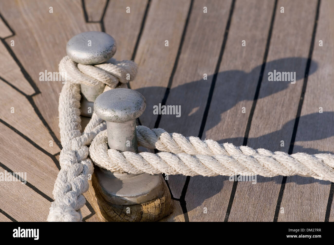 Détail d'un pont de bateau en teck : cordes attaché sur un bitt Banque D'Images