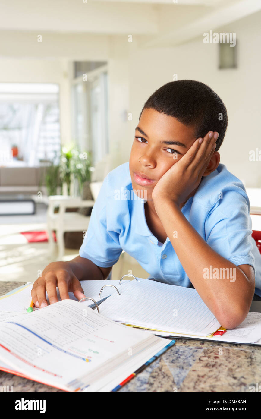 Fed Up Boy Doing Homework in Kitchen Banque D'Images