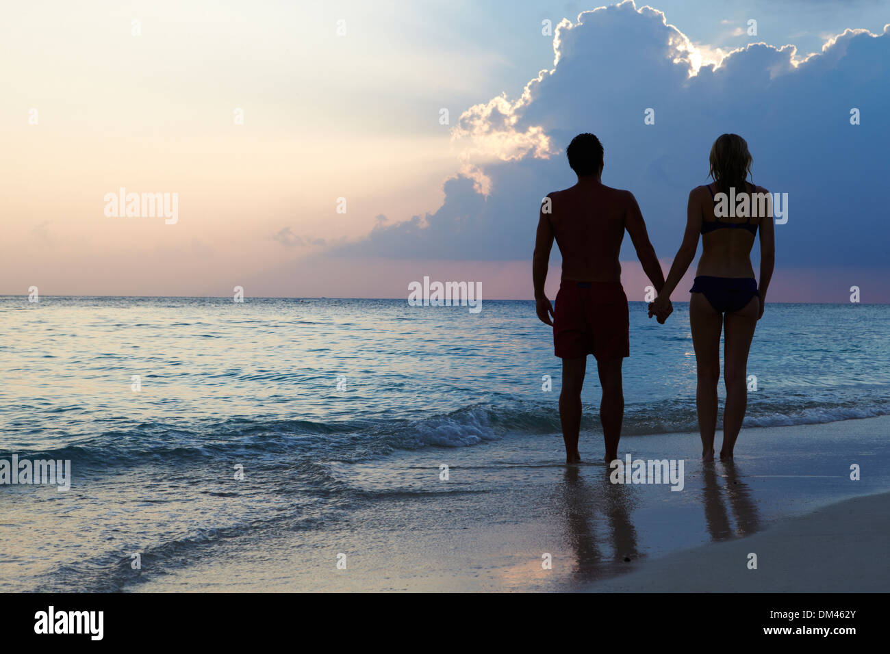 Silhouette de couple en train de marcher le long de plage au coucher du soleil Banque D'Images