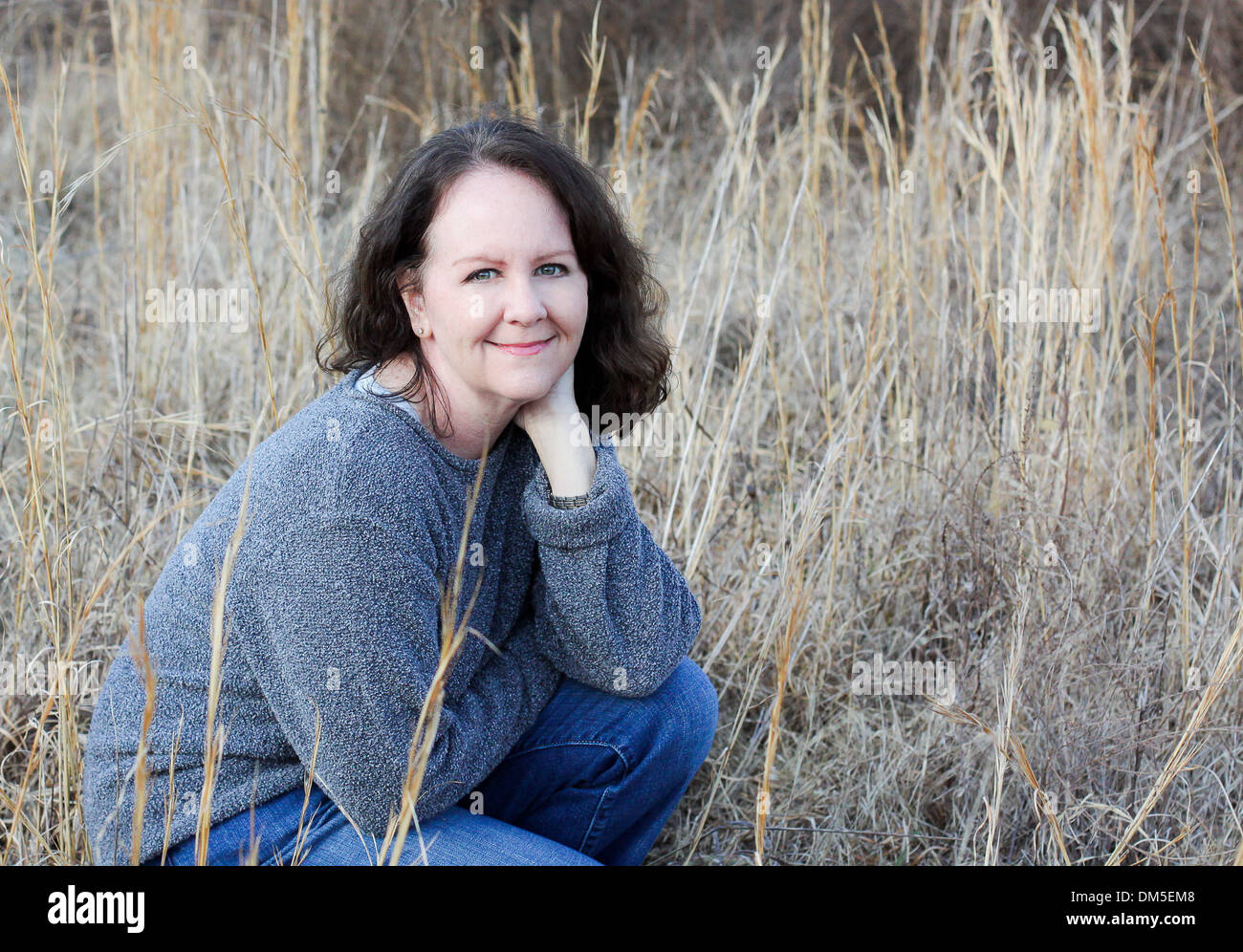 La beauté dans les hautes herbes -orientation horizontale d'une seule femme heureux et souriants qui est à genoux dans l'herbe Banque D'Images