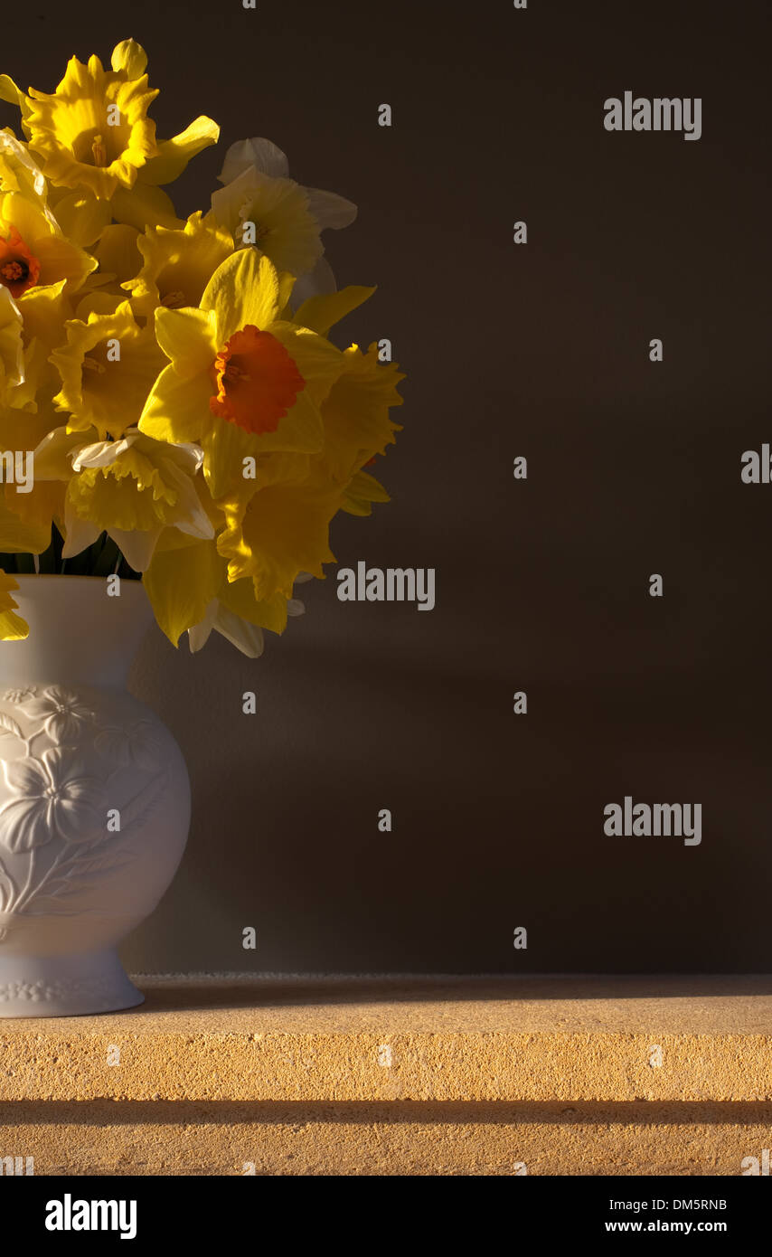 Les jonquilles dans un vase blanc sur une cheminée en pierre de Cotswold contre un arrière-plan. Banque D'Images
