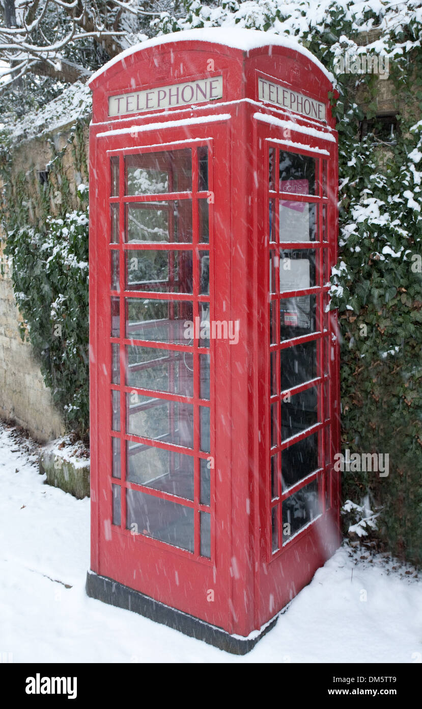 Téléphone rouge anglais fort en neige de l'hiver contre un mur en pierre de Cotswold recouvert de lierre. Banque D'Images