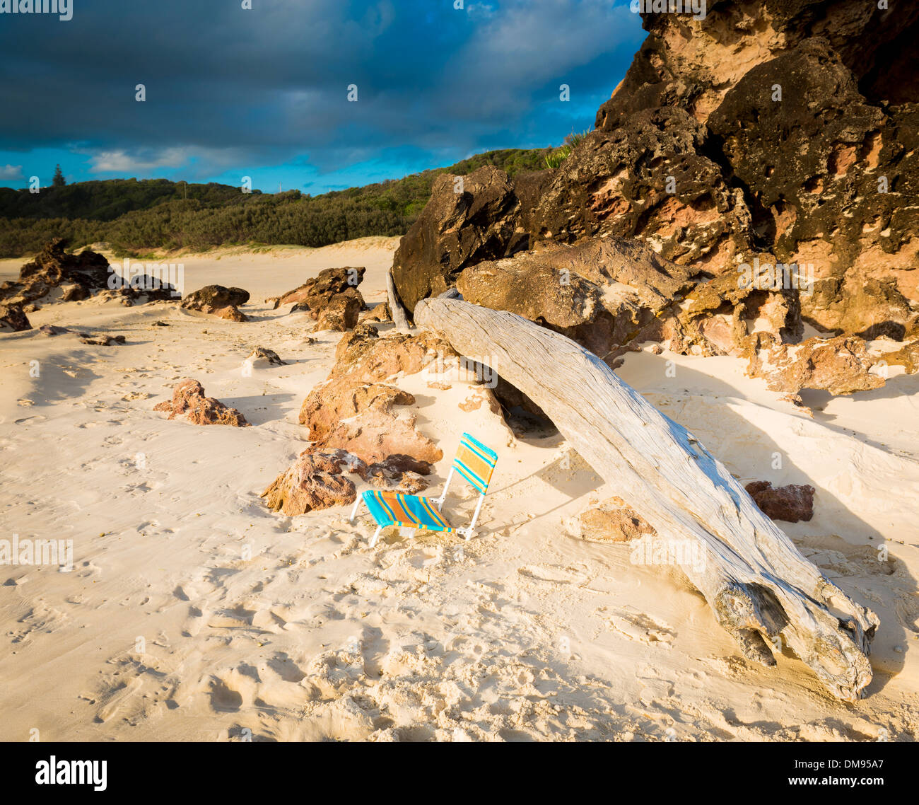 Chaise de plage vieux plantés dans le sable au lever du soleil en face d'un énorme morceau de bois flotté Banque D'Images