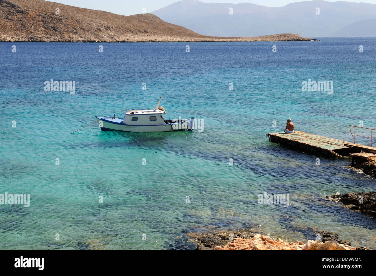 Bateau de pêche de Halki traditionnel à côté d'une jetée en bois et crystal clear blue sea beach Ftenagia Chalki île grecque La Grèce Banque D'Images