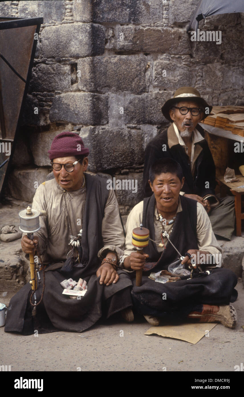 Deux vieux hommes mendier de l'argent dans une rue de Lhassa, Tibet, Chine, tournant leurs prières, et un vieil homme est la vente des Ecritures. Banque D'Images