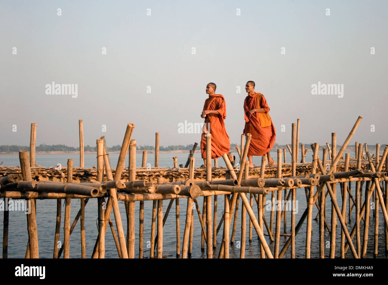 Deux moines bouddhistes portant des robes safran orange marchent sur un pont de bambou sur la rivière du Mékong à Kampong Cham, au Cambodge. Banque D'Images