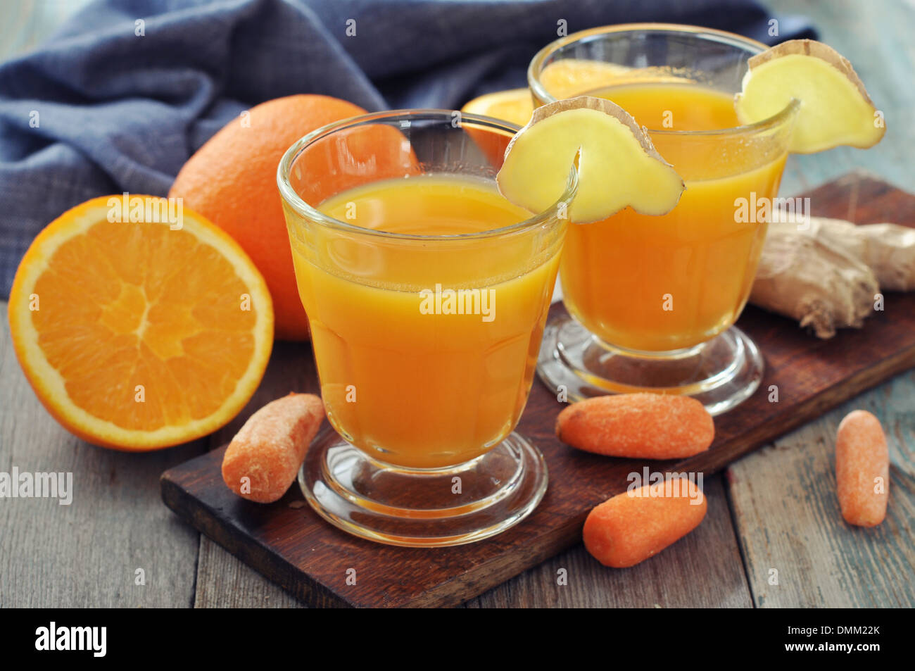 L'orange et le jus de carotte dans le verre avec du gingembre, des légumes frais et fruits sur fond de bois Banque D'Images