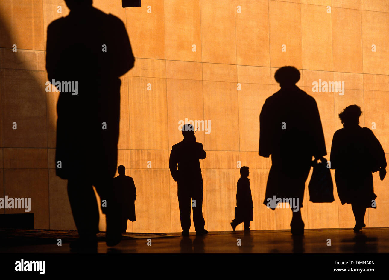 Au cours de l'heure de pointe du matin, six employés de bureau silhouette sur le grand mur d'orange d'un bâtiment municipal. Banque D'Images