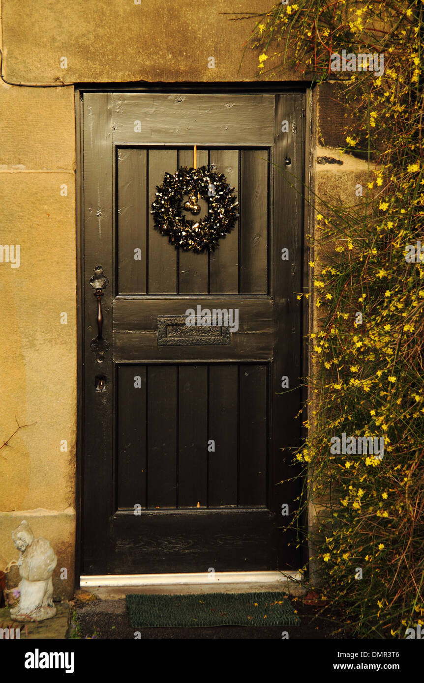 Couronne de Noël accroché sur la porte d'un "fouet cottage" flanquée de jasmin, fleurs d'hiver ; Derbyshire, Royaume-Uni Eyam Banque D'Images