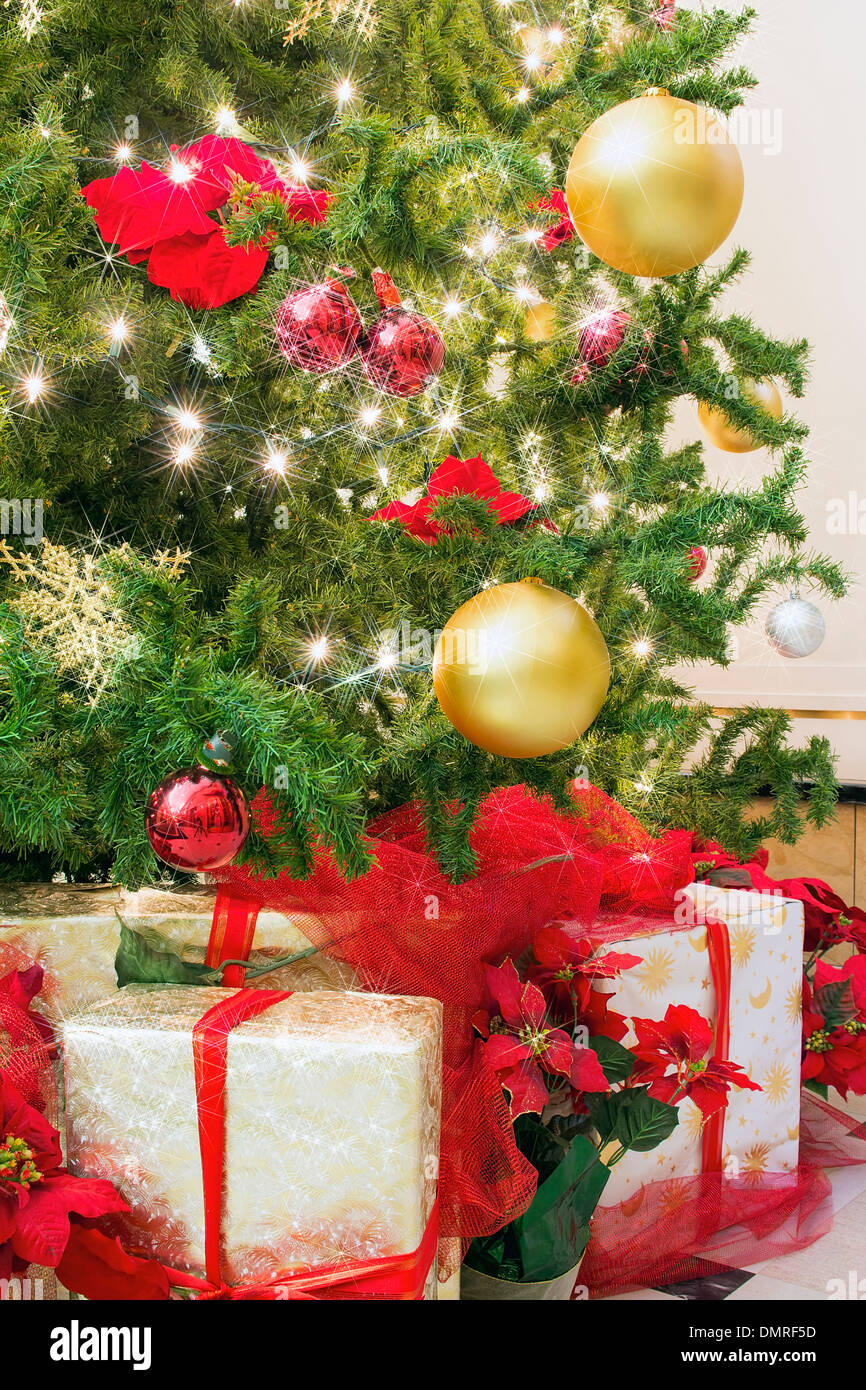 Arbre de Noël décoré avec des lumières scintillantes Poinsettia Ornements Snowflakes avec les cadeaux emballés sous l'arbre Banque D'Images