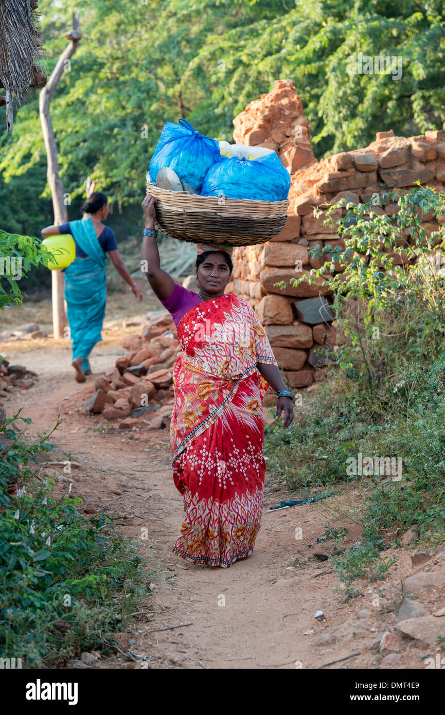 Village de l'Inde rurale femme transportant un panier contenant des sachets de fleurs sur sa tête dans un village indien. L'Andhra Pradesh, Inde Banque D'Images
