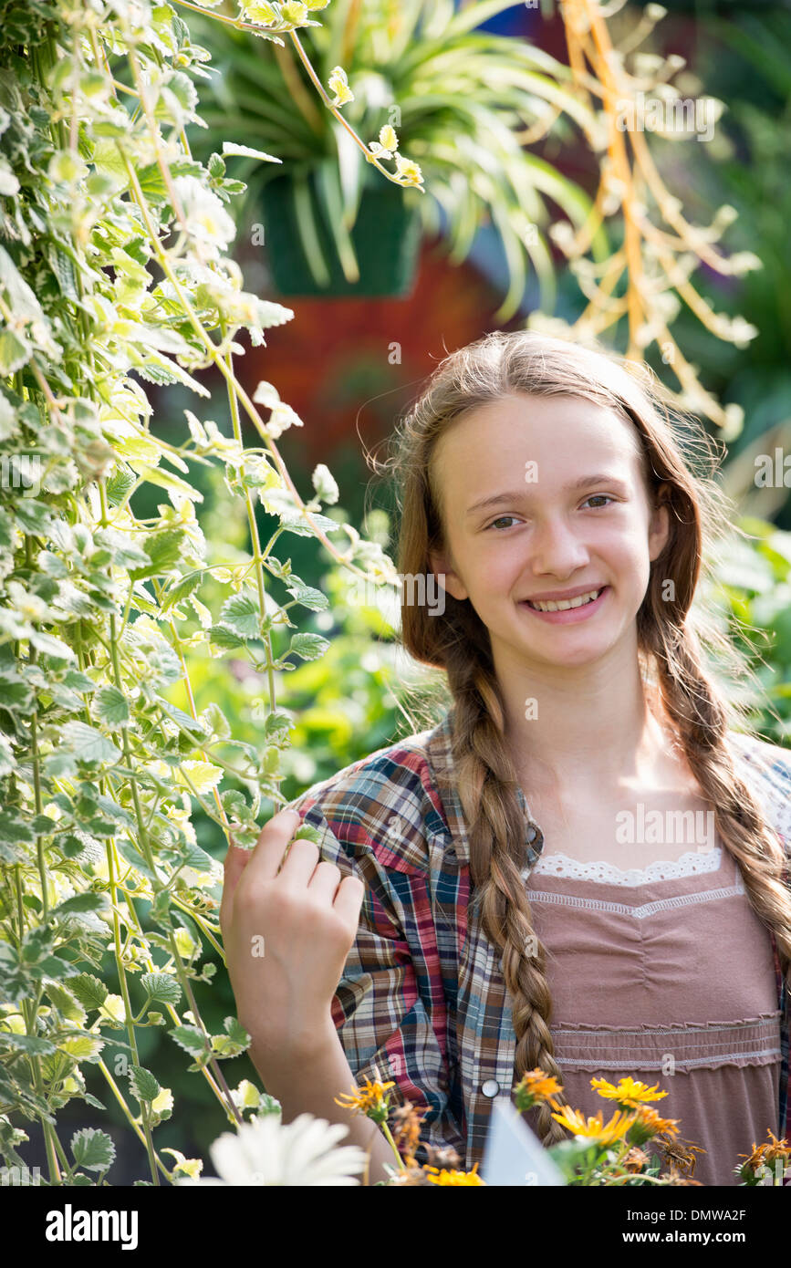 L'été sur une ferme biologique. Une jeune fille dans une pépinière pleine de fleurs. Banque D'Images