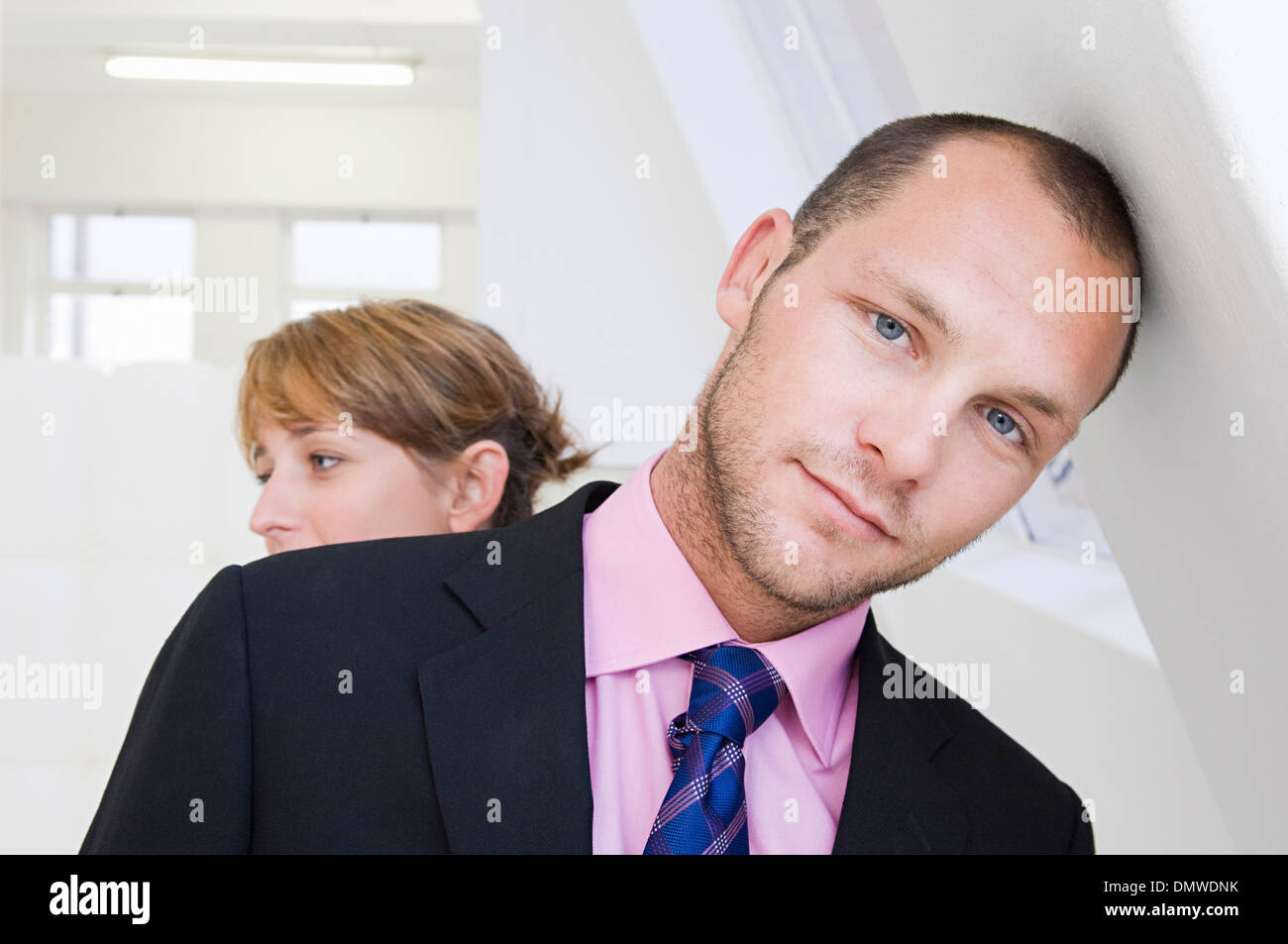 Un jeune homme en costume et chemise rose appuyé contre un mur et une jeune  femme en arrière-plan Photo Stock - Alamy