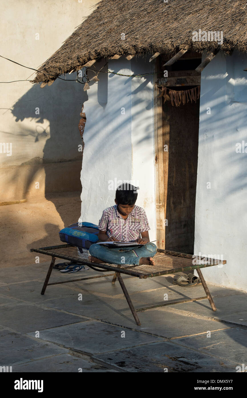 Jeune Indien garçon faire le travail scolaire en dehors de son village de l'Inde rurale accueil. L'Andhra Pradesh, Inde Banque D'Images