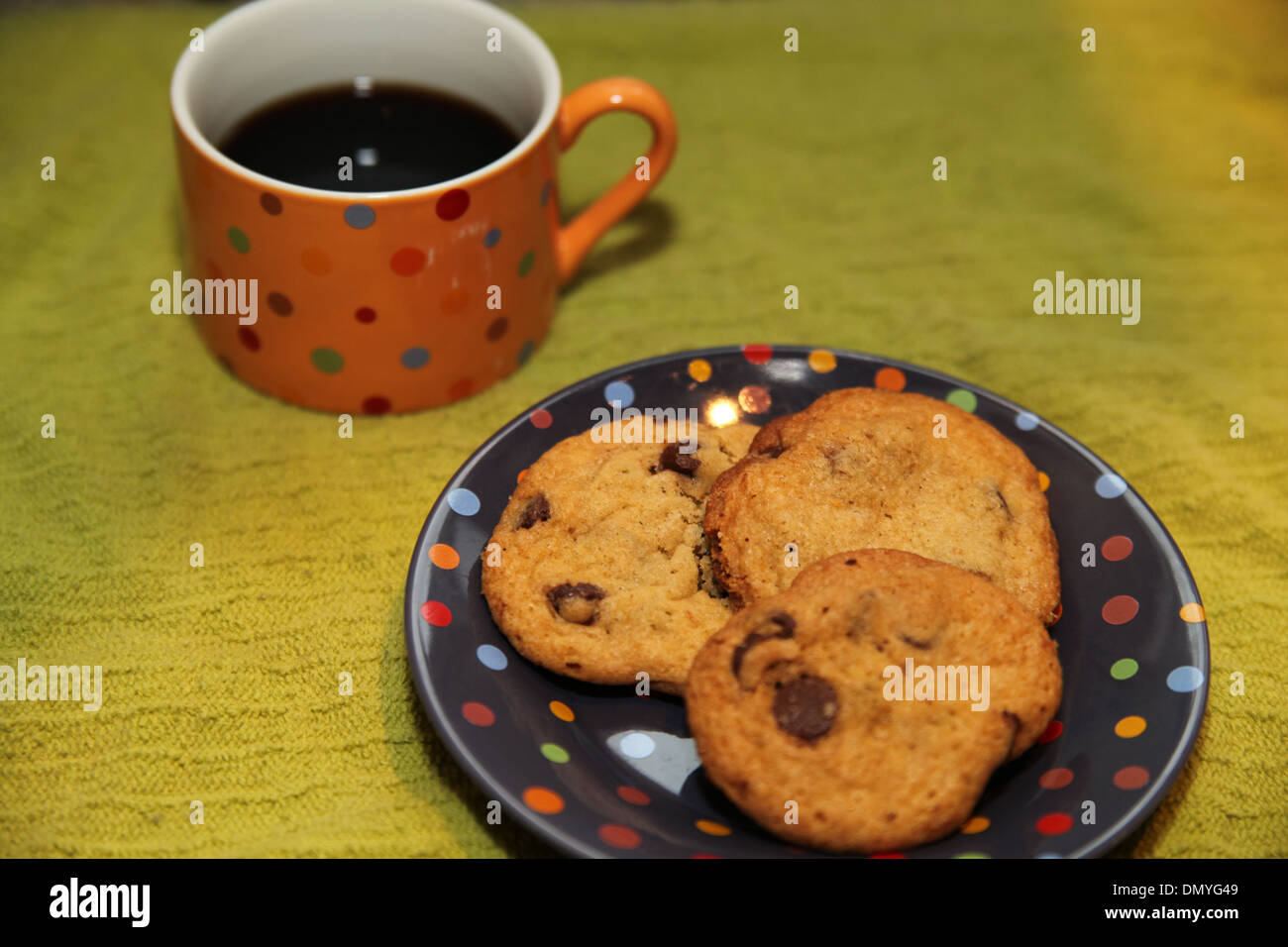 Une tasse de café noir avec trois cookies aux pépites de chocolat sur une plaque à pois Banque D'Images