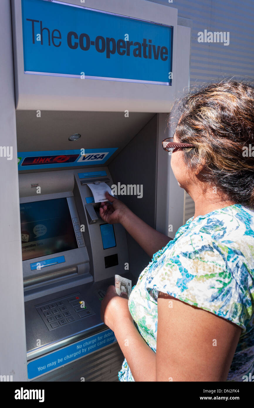 Middle-aged Hispanic woman withdrawing l'argent d'une banque coopérative ATM machine en Angleterre, FR, UK. Banque D'Images