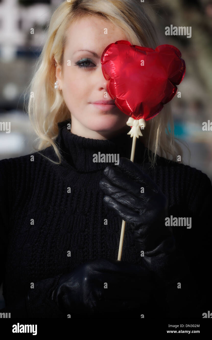 Une fille blonde tient un ballon en forme de coeur en face de l'œil Banque D'Images