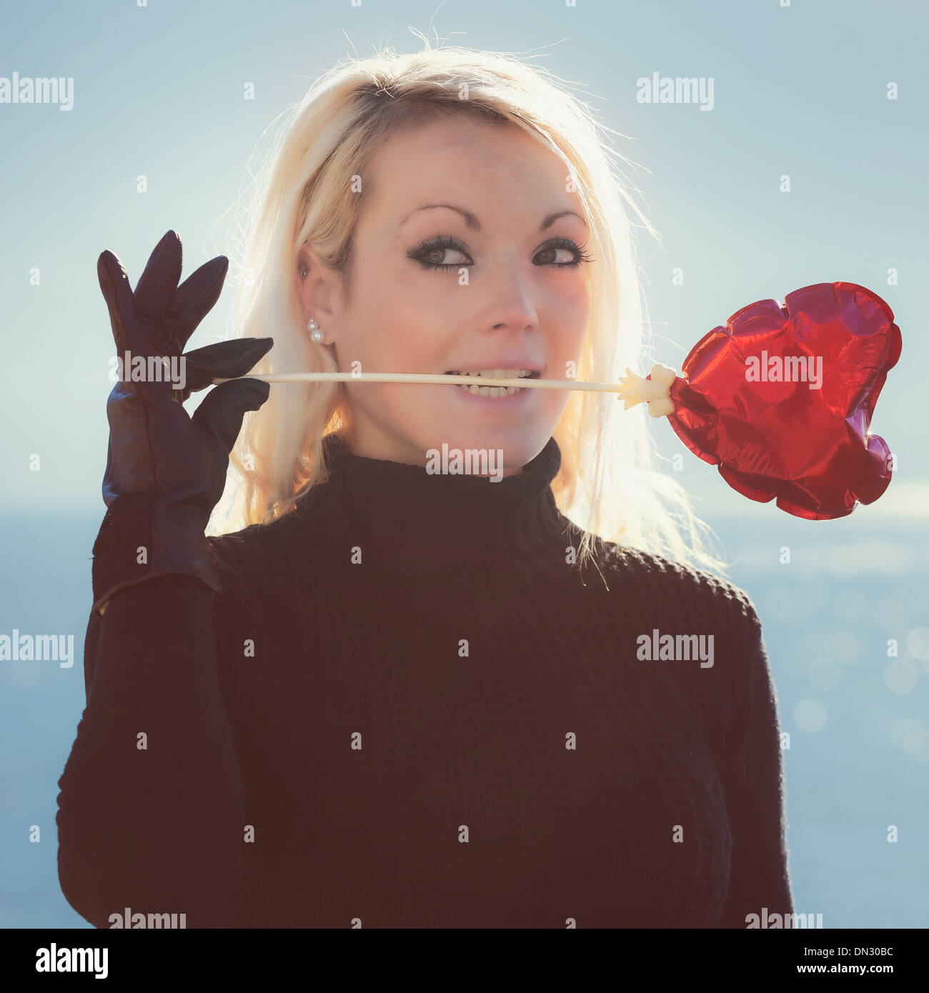 Une fille blonde tient un ballon en forme de coeur dans sa bouche Banque D'Images