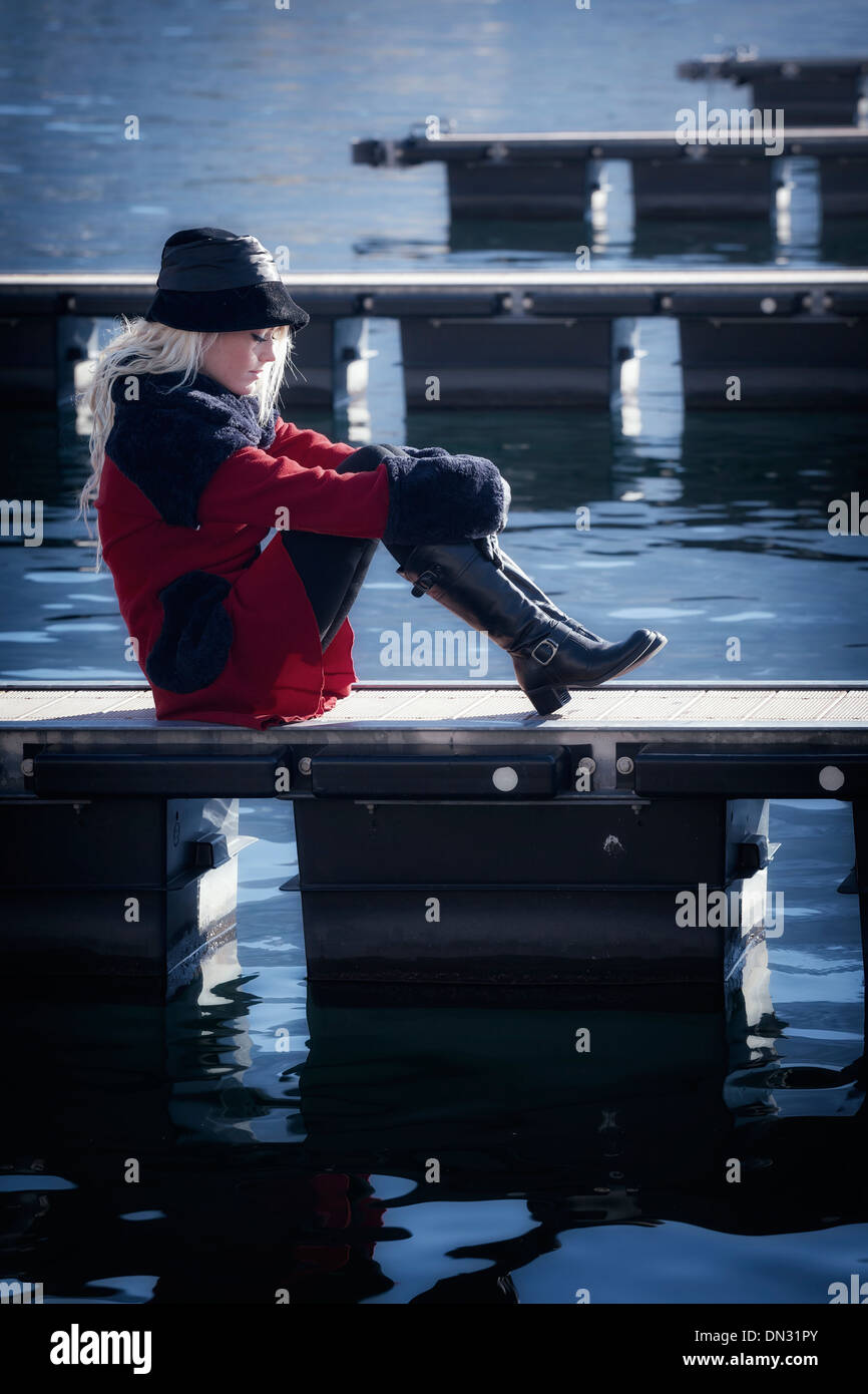 Une femme dans un manteau rouge est assis sur une jetée Banque D'Images