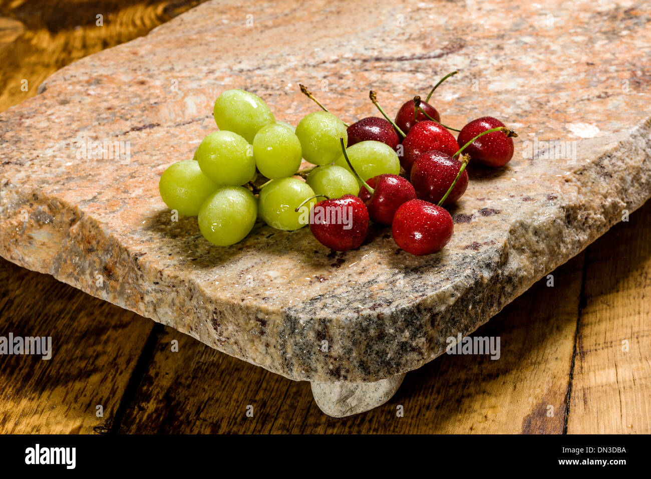 Les fruits, les raisins et les cerises, sur une dalle de granit recyclé servant. Banque D'Images