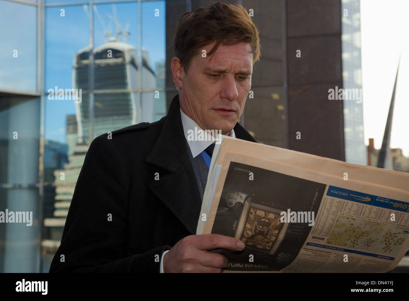 Une ville de Londres à la recherche d'affaires inquiets et froncer pendant qu'il lit le Financial Times avec le 'talkie walkie' derrière lui Banque D'Images