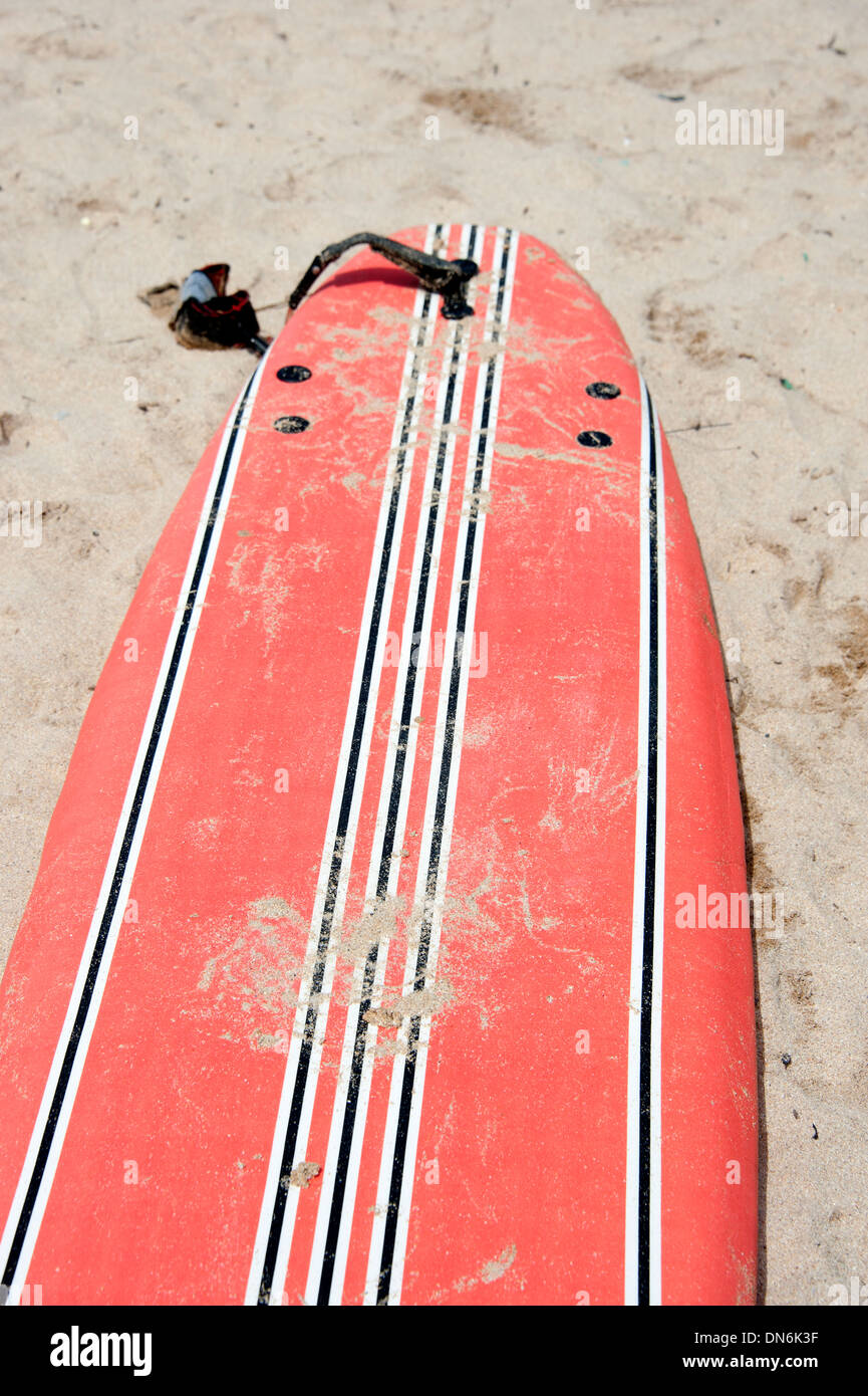 Conseil de surf orange vif couvert de sable sur plage Banque D'Images