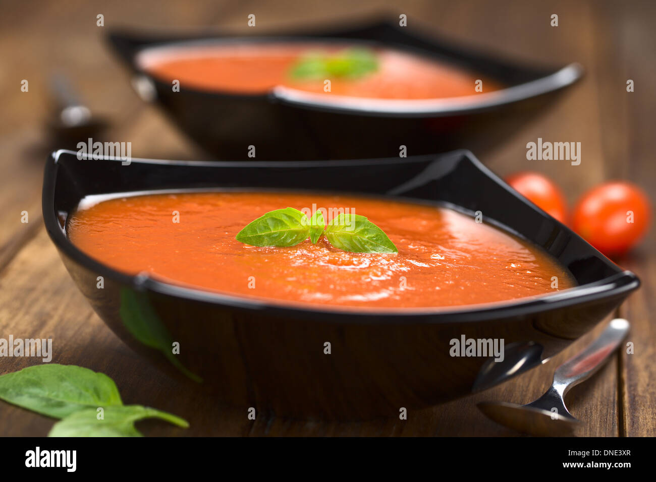 Soupe de tomates fraîches faites maison avec des feuilles de basilic sur le dessus servi dans un bol en bois foncé sur noir Banque D'Images