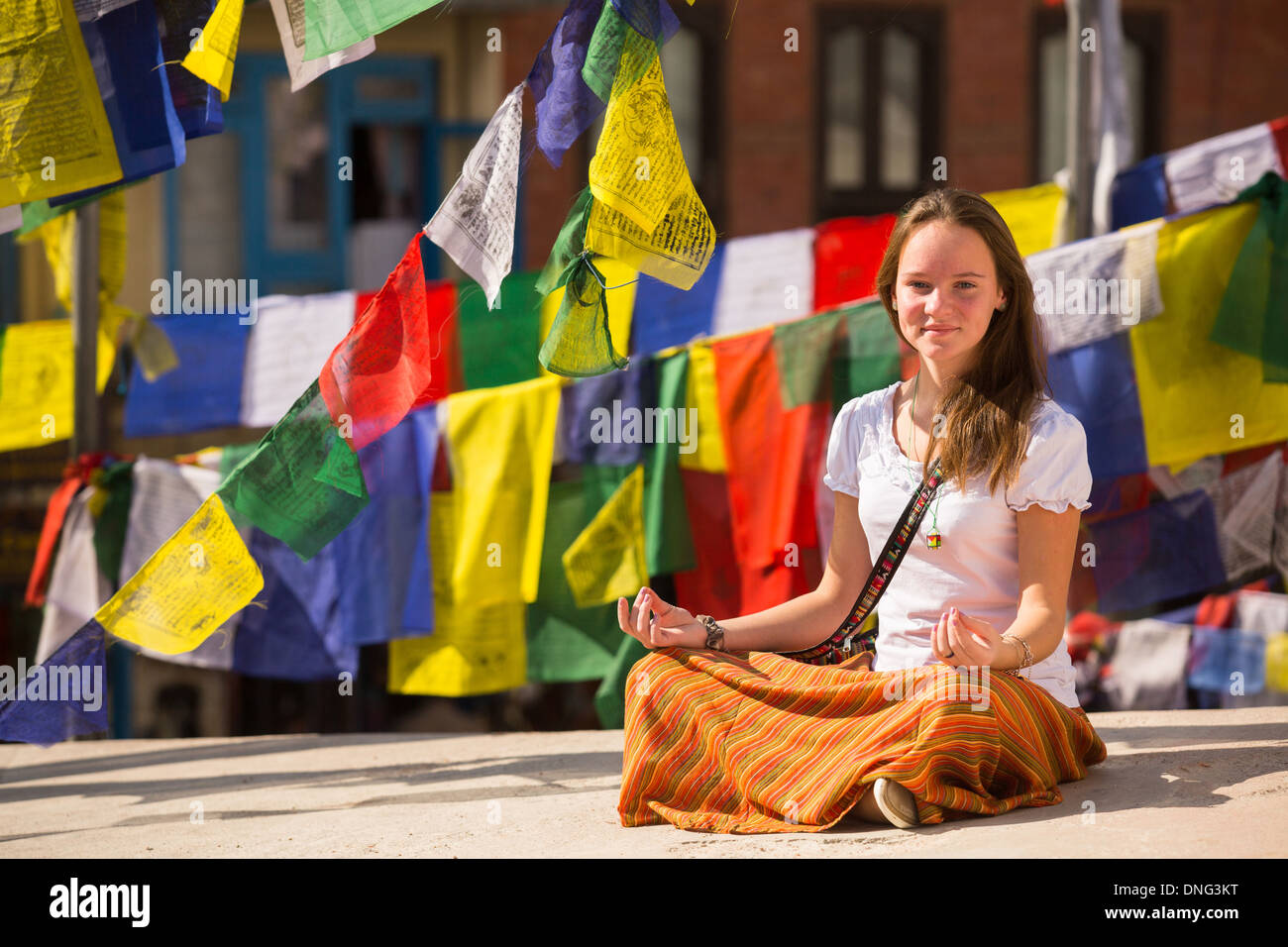 Jeune fille assise dans la position du lotus sur la prière, stupa bouddhiste drapeaux flottants à l'arrière-plan. Banque D'Images