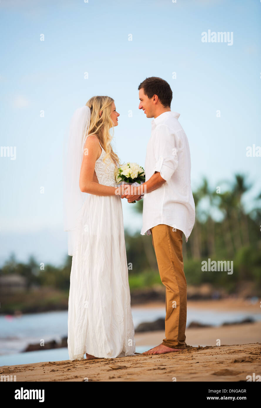 Juste married couple holding hands sur la plage au coucher du soleil, moment d'amour intime au mariage Banque D'Images