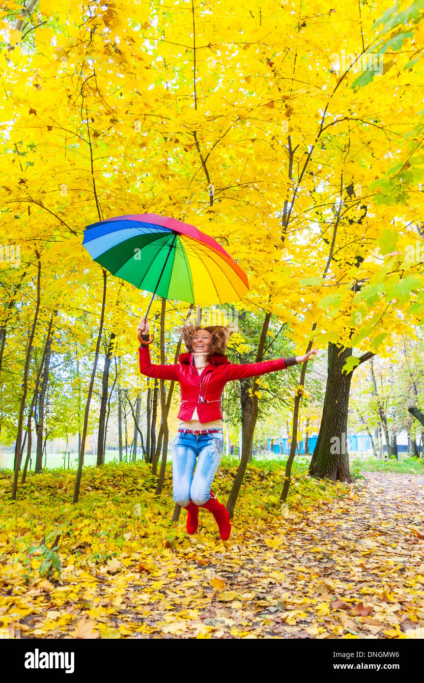 Jolie fille avec un parapluie multicolore jumping in autumn park Banque D'Images