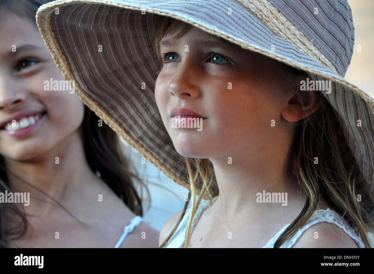Portrait de petite fille blonde jusqu'à porter un chapeau de soleil avec son amie derrière elle Banque D'Images