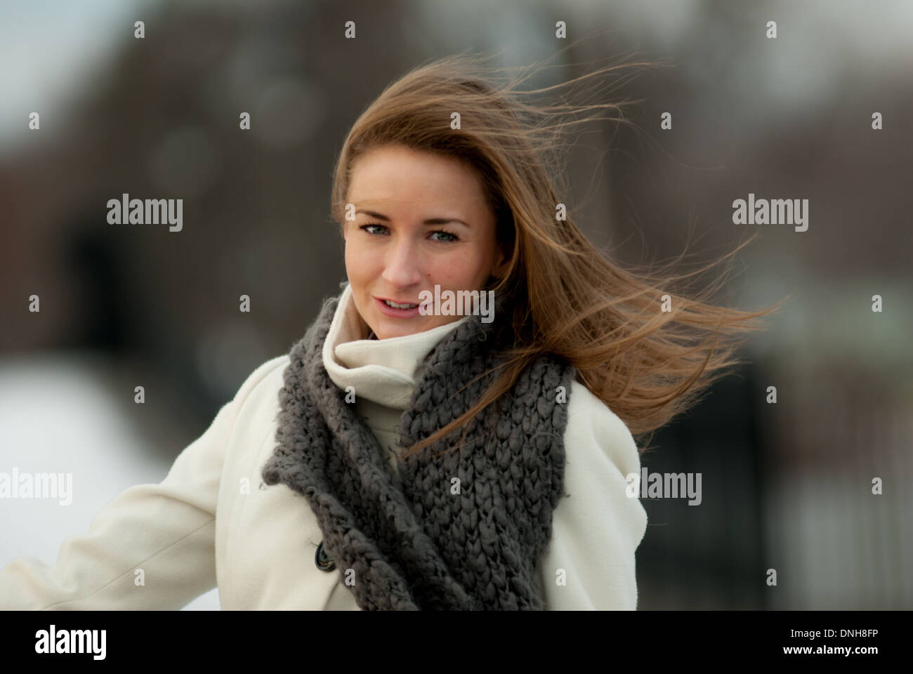 Une belle jeune femme dans une robe blanche et foulard gris sourires sur un jour d'hiver venteux. Banque D'Images