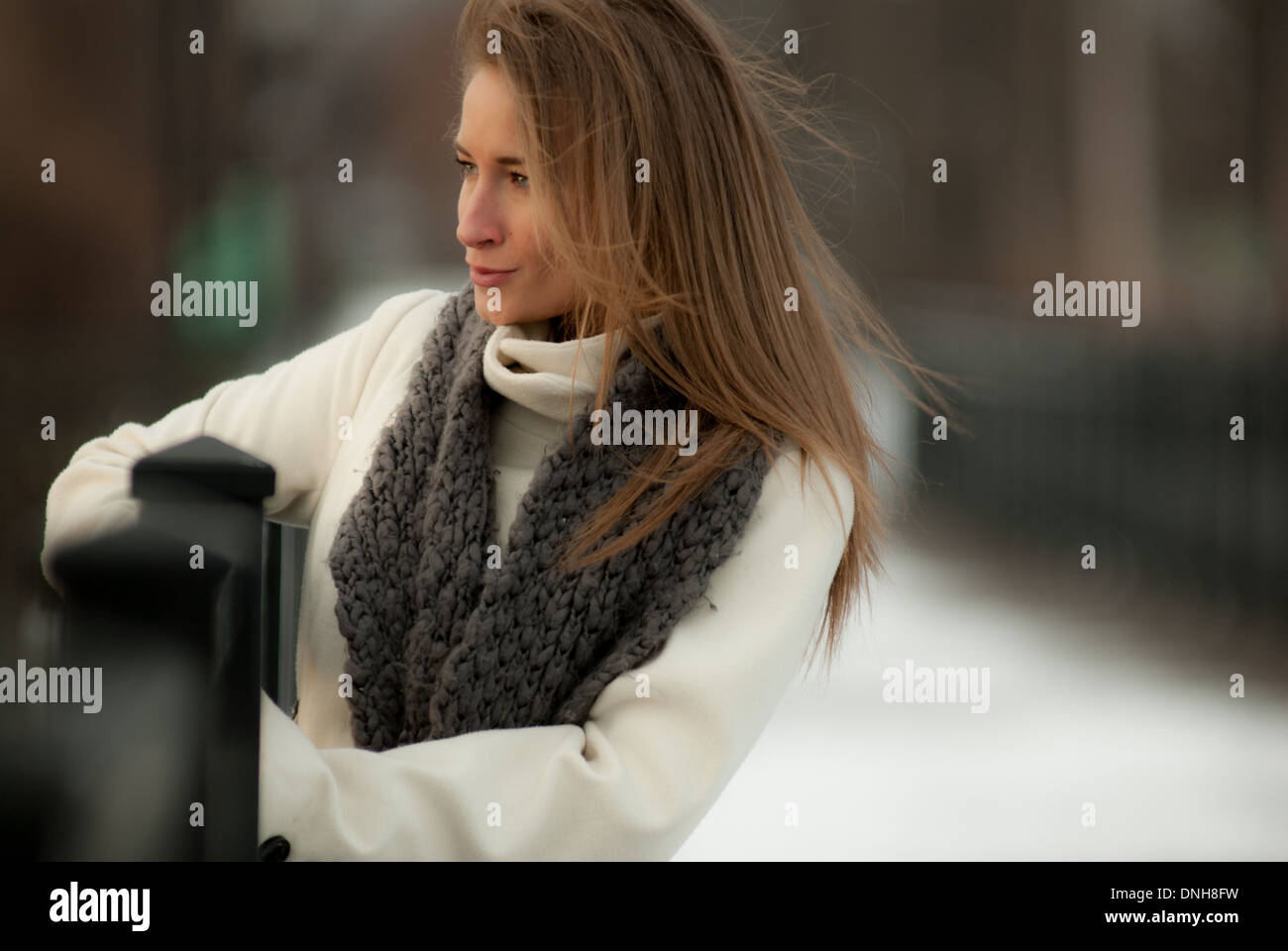 Une belle jeune femme dans une robe blanche et un foulard gris sur un pont en hiver. Banque D'Images