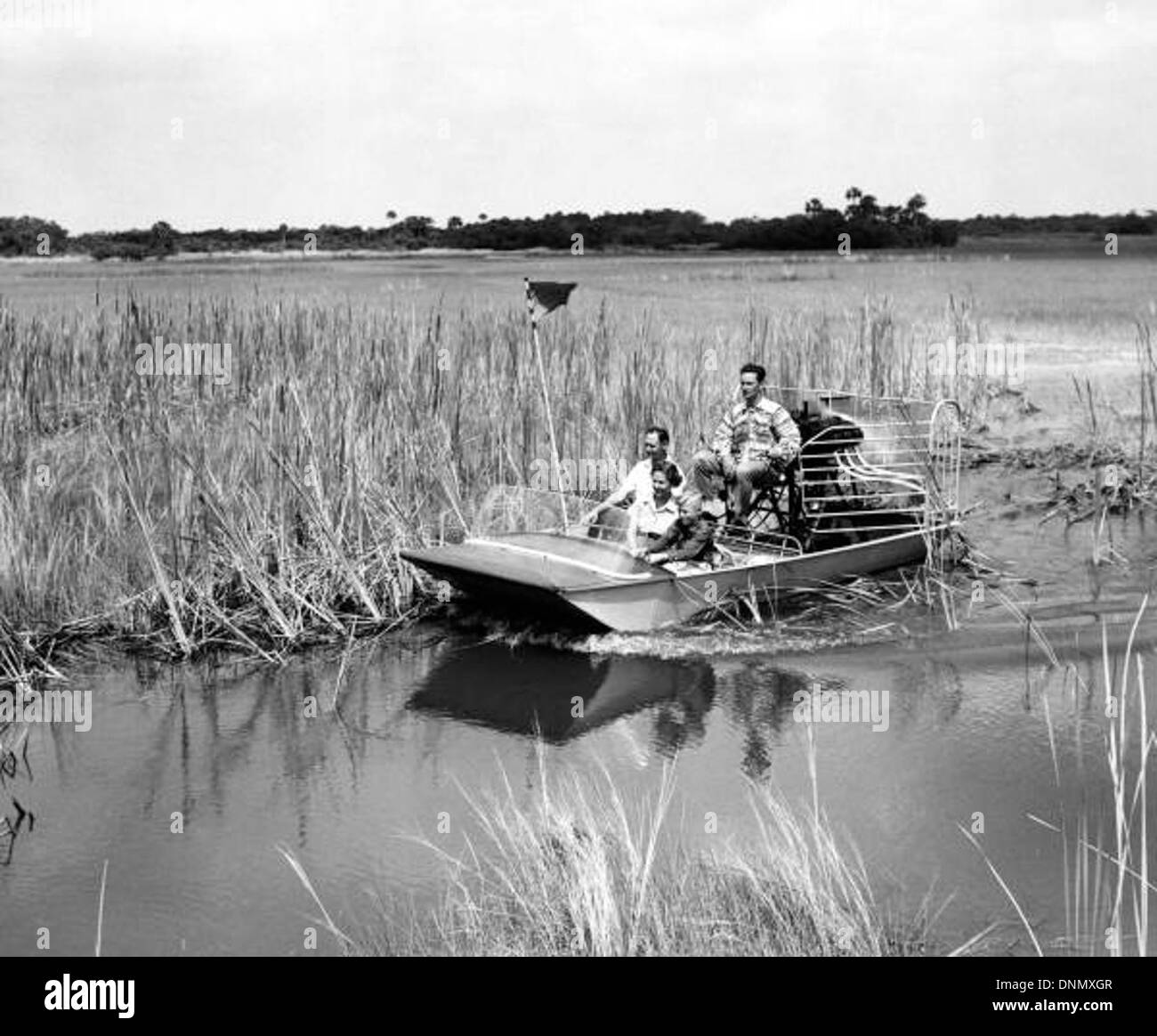 La famille Landers embarque pour une excursion en hydroglisseur dans le parc national des Everglades, capturant le paysage unique des marécages, des roseaux et de la scierie dans les années 1950 L’image reflète les loisirs familiaux dans l’environnement naturel de la Floride. Banque D'Images