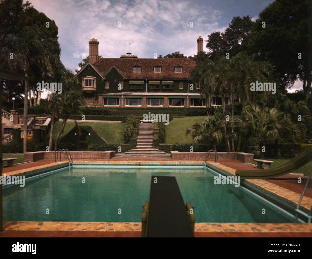 Un manoir des années 1960 à Sarasota, en Floride, photographié à partir de la collection Joseph Janney Steinmetz, mettant en valeur l'architecture, l'aménagement paysager et les caractéristiques de la piscine de l'époque. L'image met en évidence des palmiers, des plongeons et des toboggans aquatiques, reflétant le design luxueux des maisons de Floride. Le comté de Sarasota est l'emplacement du manoir, conservé dans la Bibliothèque d'État et les Archives de Floride. Banque D'Images