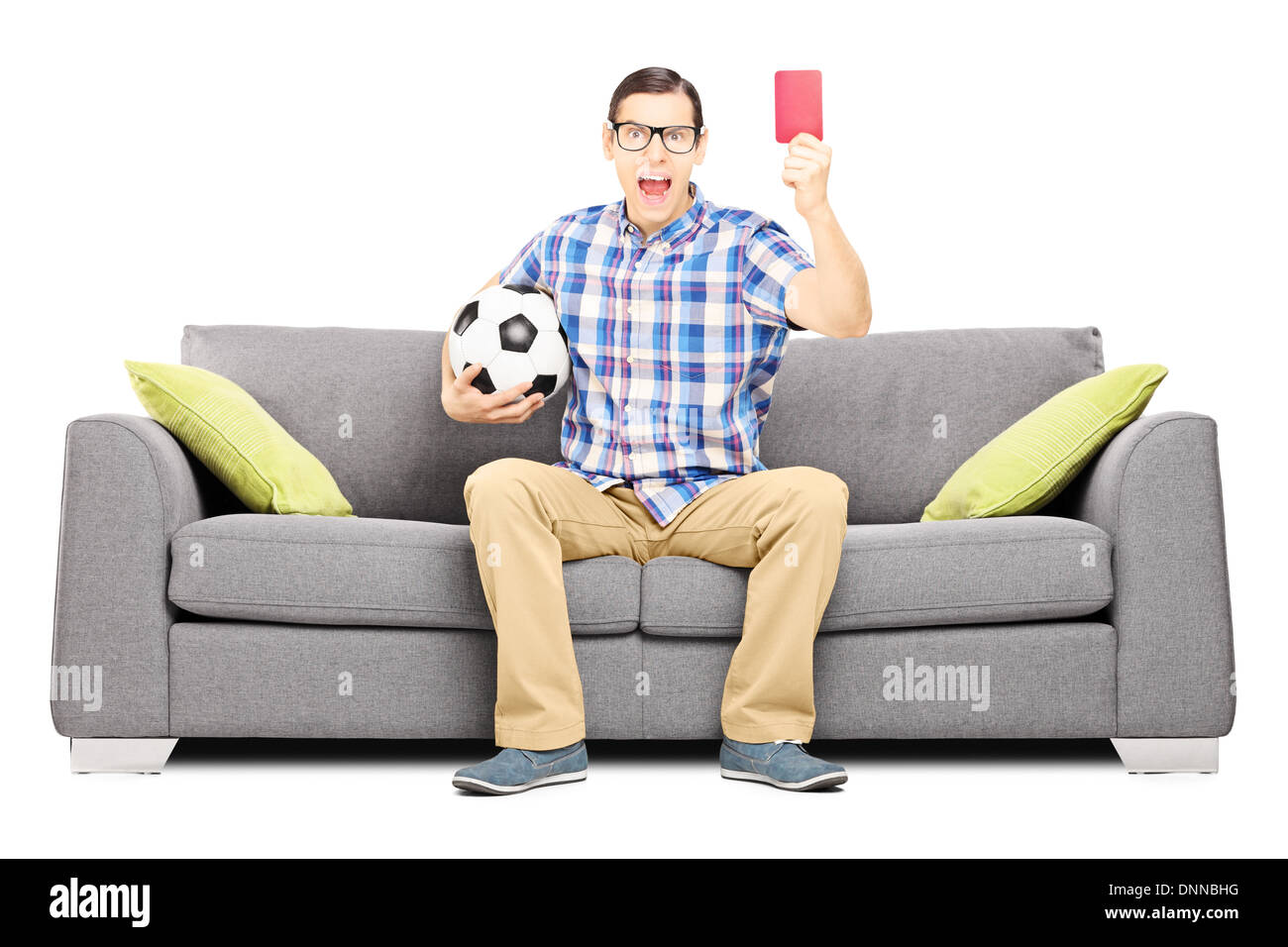 Les jeunes furieux fan de football sitting on sofa holding ball et donner une carte rouge Banque D'Images