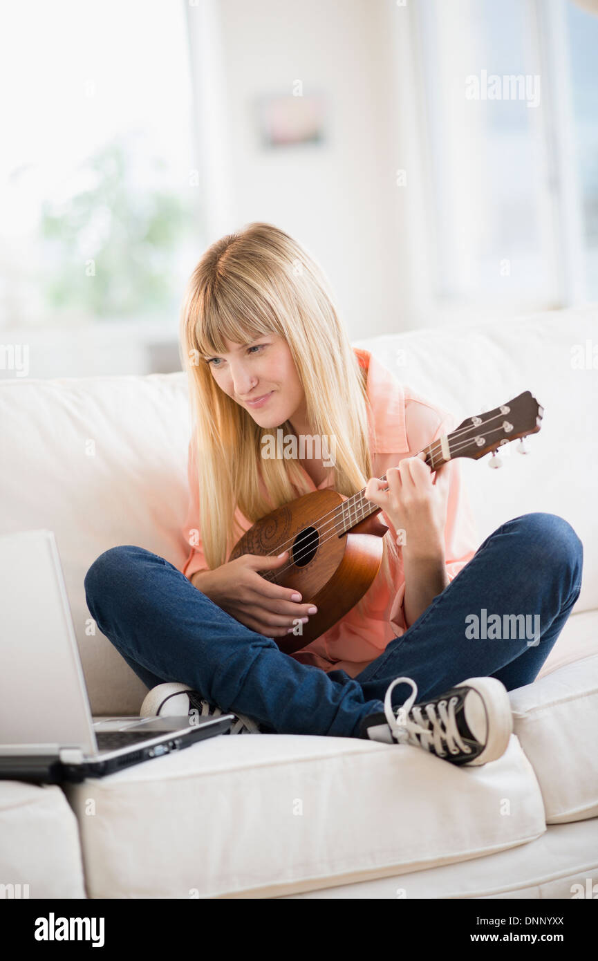 Femme jouant de ukulele while using laptop Banque D'Images