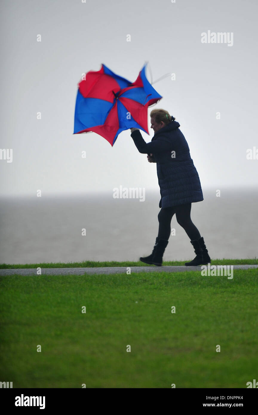 Une femme luttant contre le vent avec un parapluie dans l'île de Barry, au Pays de Galles, Royaume-Uni. Banque D'Images