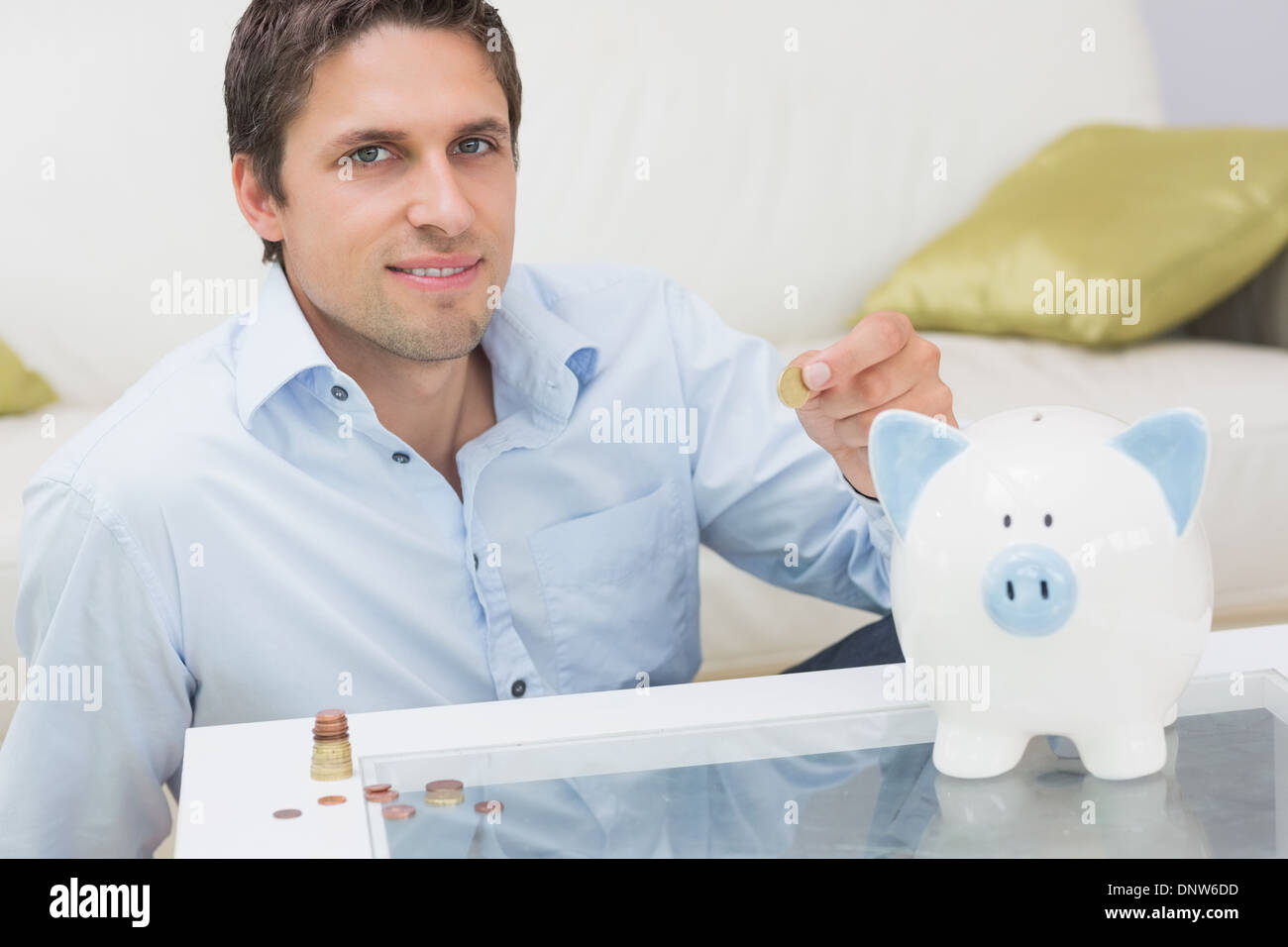 Casual man mettre quelques pièces de monnaie dans une tirelire dans la salle de séjour Banque D'Images