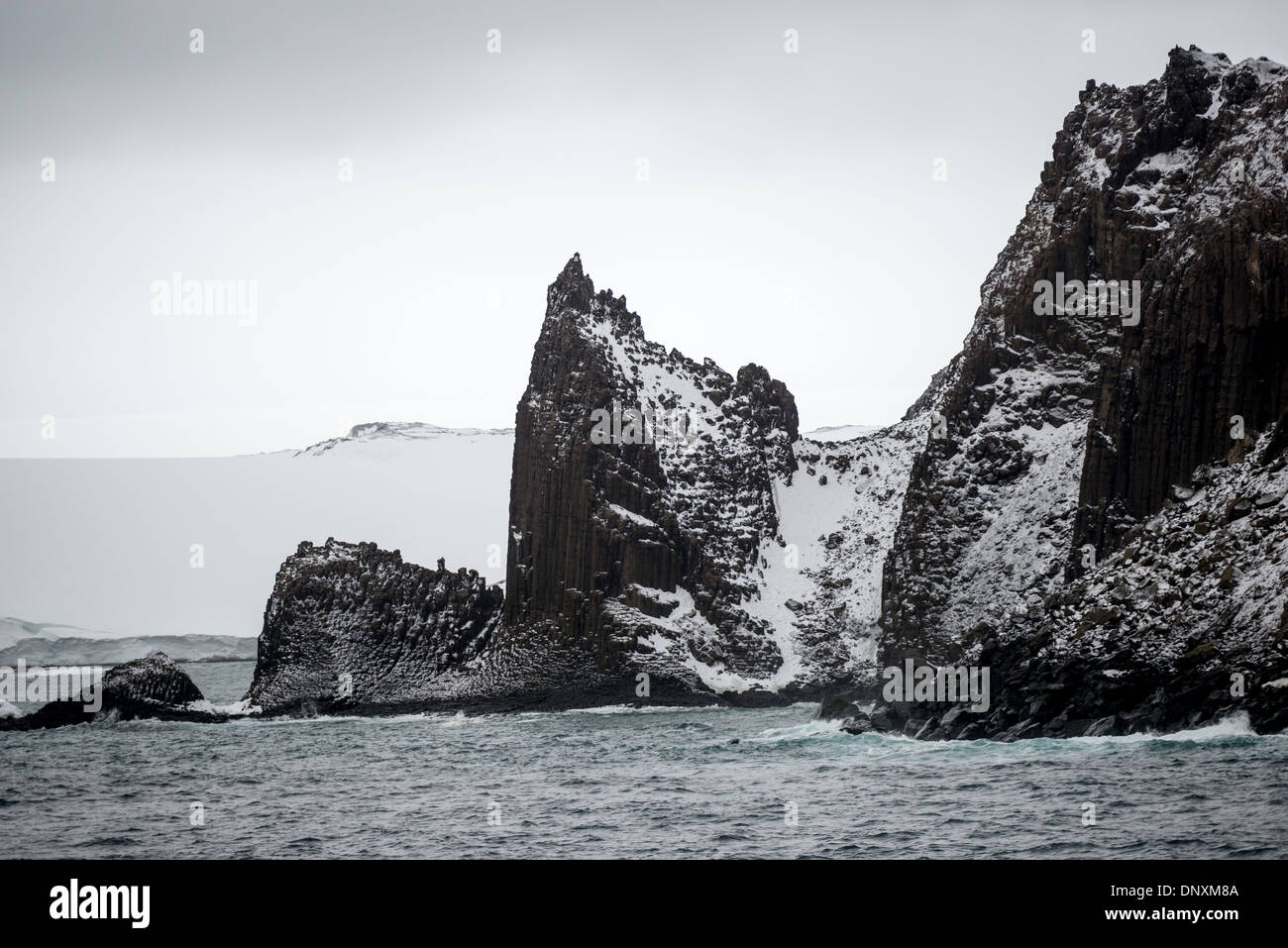 Îles South Shetland Paysage accidenté Antarctique | ENGLISH STRAIT, Antarctique — Des colonnes de basalte striées de neige s'élèvent de l'île Robert au-dessus de l'English Strait dans les îles South Shetland, un terrain resté largement inchangé depuis que les chasseurs de phoques ont suivi la découverte de William Smith en 1819 ici. Son rapport sur les colonies denses de phoques a déclenché une ruée qui a conduit le phoque à fourrure antarctique presque à l'extinction en quelques saisons ; l'espèce s'est depuis rétablie grâce aux protections du Traité antarctique. Banque D'Images