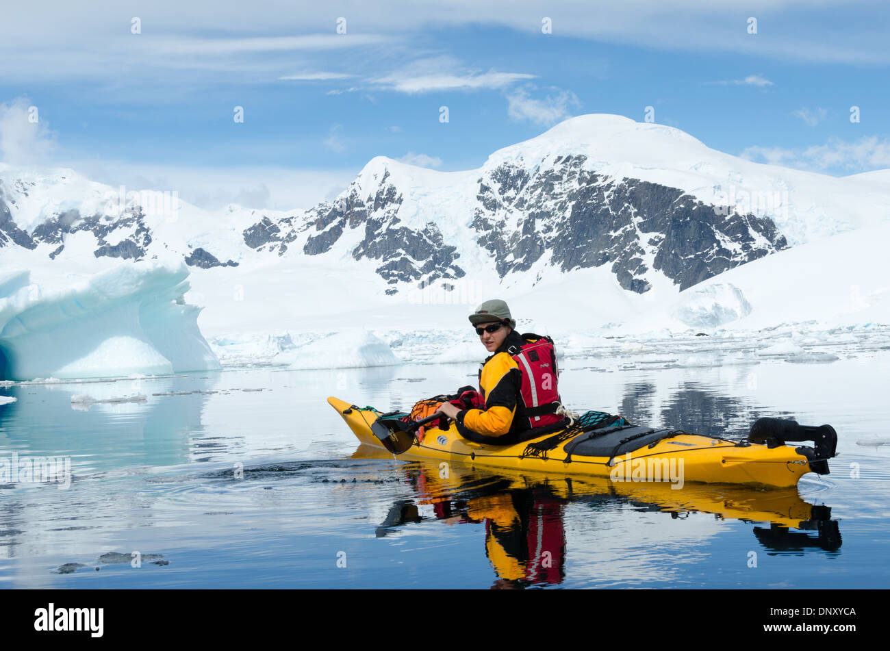 Un kayakiste solo sur les eaux encore vitreux à Cuverville Island sur la péninsule Antarctique, avec de grandes montagnes enneigées en arrière-plan. Banque D'Images