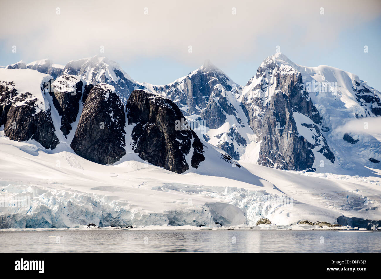Petermann Island montagnes enneigées Antarctique // PETERMANN ISLAND, Antarctique — Une vue panoramique des montagnes rocheuses abruptes et enneigées vues depuis l'île Petermann en Antarctique. L'île est connue pour ses falaises rocheuses spectaculaires bordées de glace et de neige, offrant un contraste saisissant avec le paysage glacé environnant. D'imposantes falaises dominent la scène, soulignant la beauté sauvage de cet endroit reculé de l'Antarctique. Petermann Island est un endroit populaire pour observer la faune, y compris les pingouins et les phoques, que l'on trouve couramment le long de ses rives. Banque D'Images