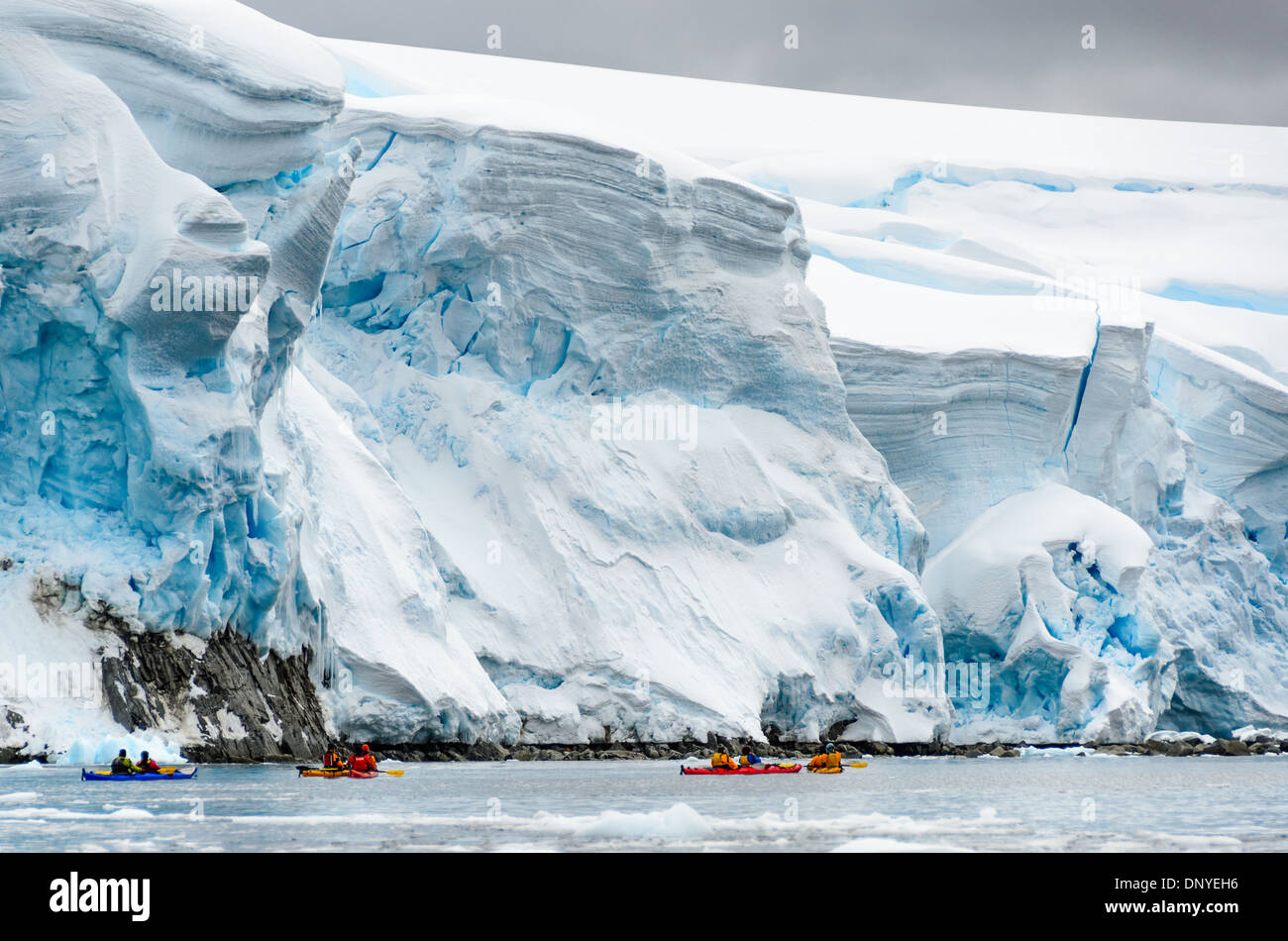 Glacial Ice Cliffs kayakistes Melchior Island Antarctica Peninsula // kayakistes pagayent devant d'énormes falaises de glace glaciaire glissant lentement dans la mer le long du front de mer à Melchior Island sur la côte ouest de la péninsule Antarctique. Banque D'Images